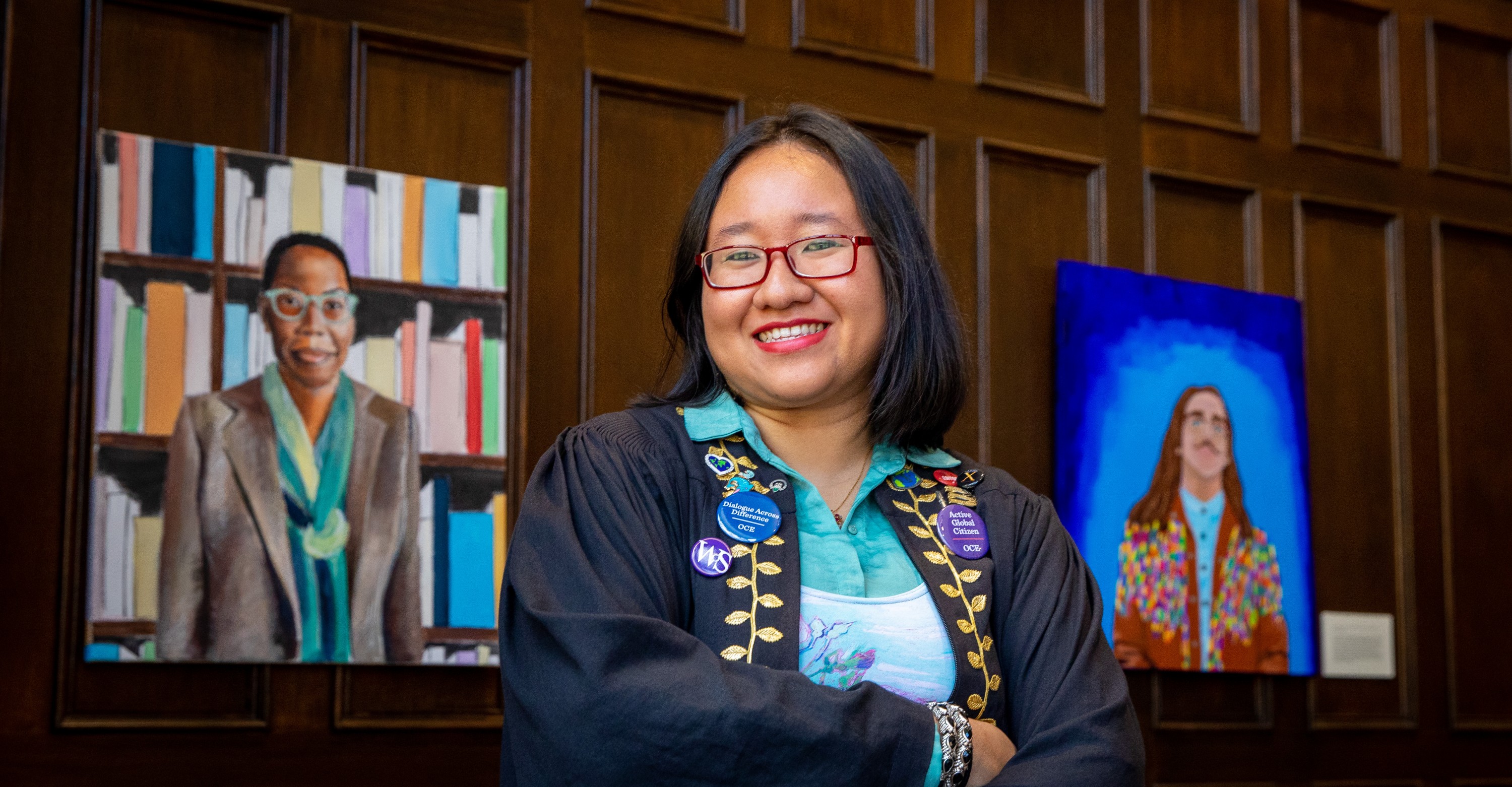 Mandy Moe Pwint Tu, C'21, stands between paintings of Cortney Thompson (left) and Levi Trumbore (right).